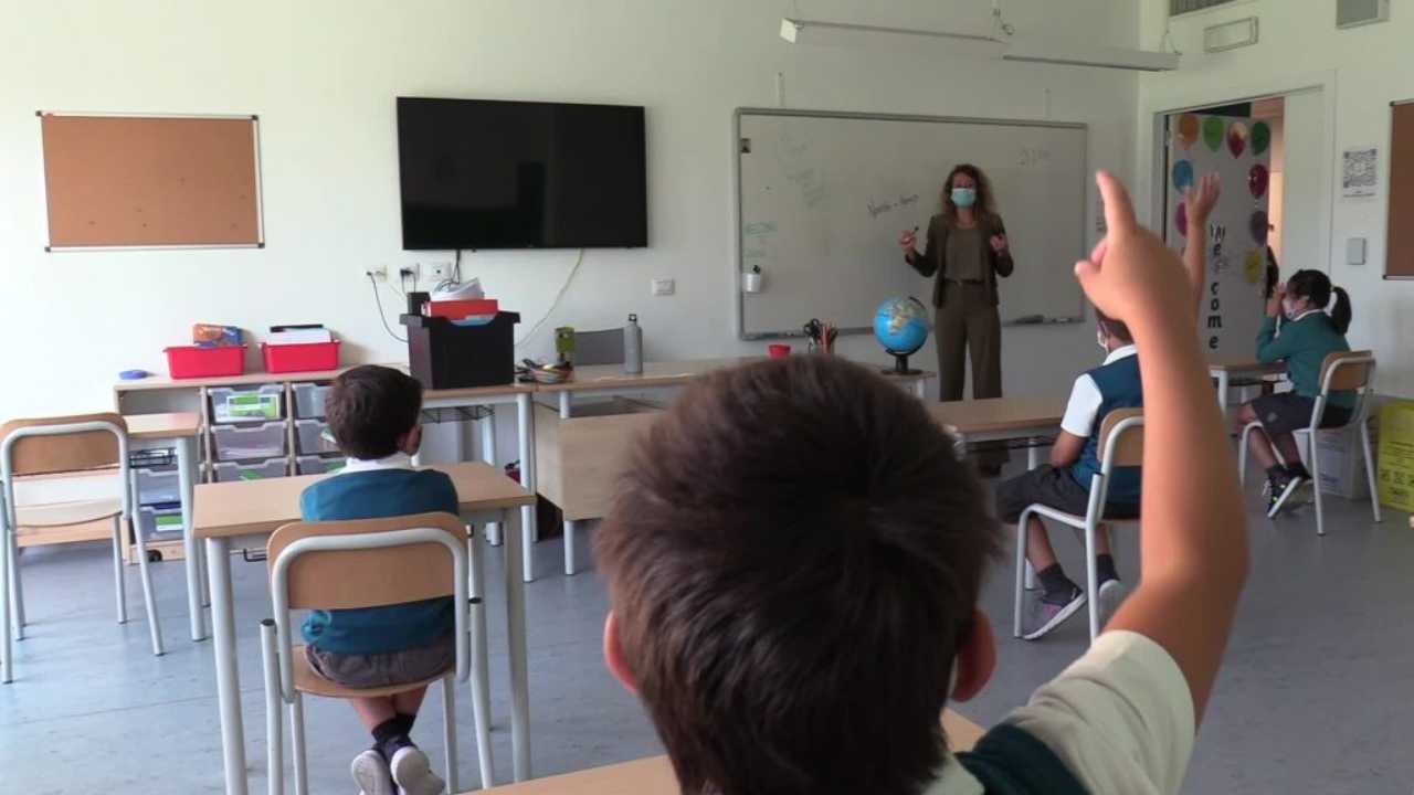 Una classe di piccoli studenti, la docente ha la mascherina