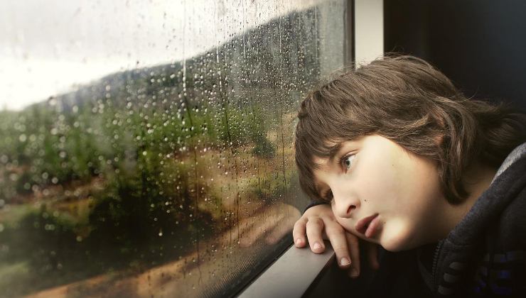 Bambino guarda la pioggia dalla finestra