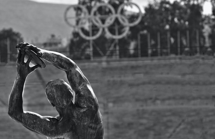 Foto in bianco e nero delle spalle della statua del discobolo di Atene, con logo delle Olimpiadi sullo sfondo