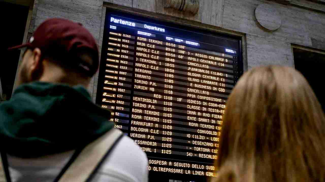 Treni sospesi, persone che guardano il tabellone in stazione