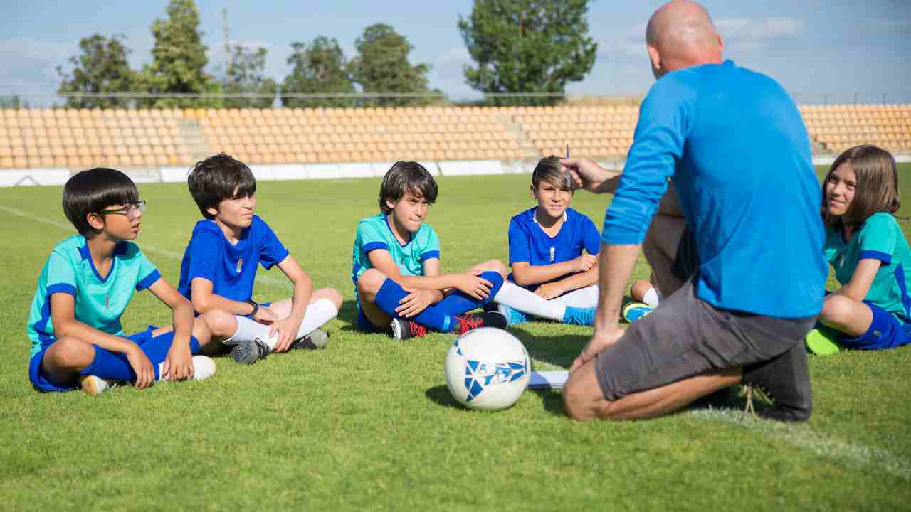 Bambini seduti su un prato da calcio ascoltano l'allenatore