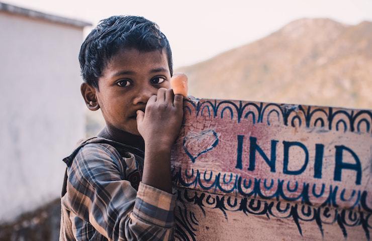 Bambino indiano appoggiato a un cartello riportante la scritta India