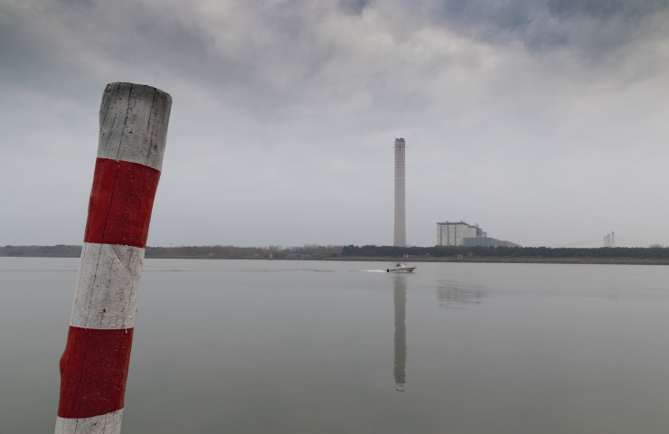 Delta del Po in una giornata nuvolosa. Barca in mezzo al fiume e industria sullo sfondo