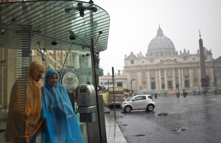 Due persone si riparano dalla pioggia sotto il tetto di una cabina telefonica a Roma