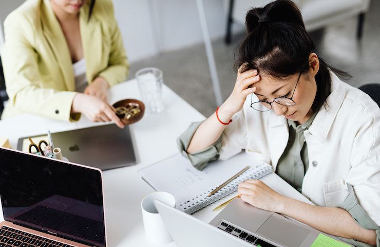 Ragazza pensierosa mentre lavora al pc in ufficio. Preoccupazione per il salario basso