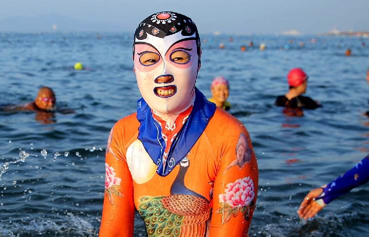 Una ragazza cinese davanti al mare che sorride indossando un facekini in fantasia nero, rosa e bianco