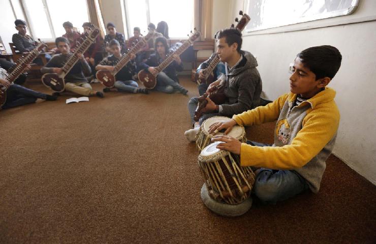 Un gruppo di giovani afgani in una classe mentre suonano degli strumenti musicali a sedere in terra