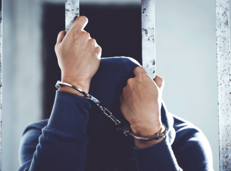 Un ragazzo con le manette appeso alle sbarre di un carcere