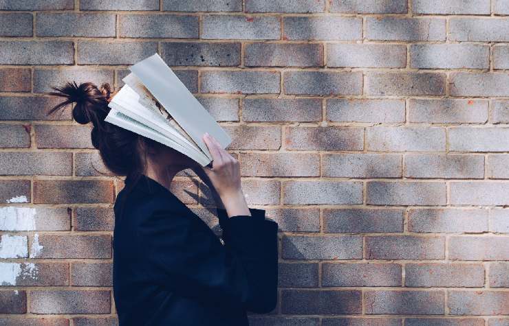 Stress da studio di una ragazza che davanti a un muro di mattoncini si copre il volto con un libro