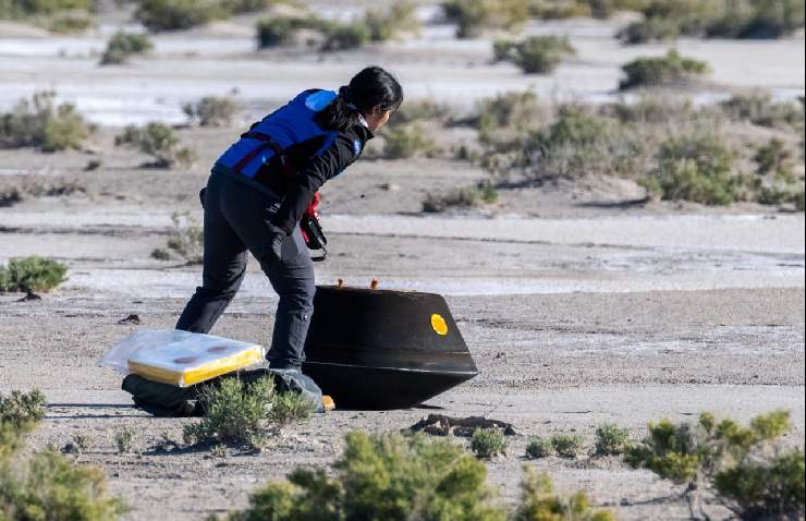 Una scienziata si avvicina ad una capsula nera nel deserto