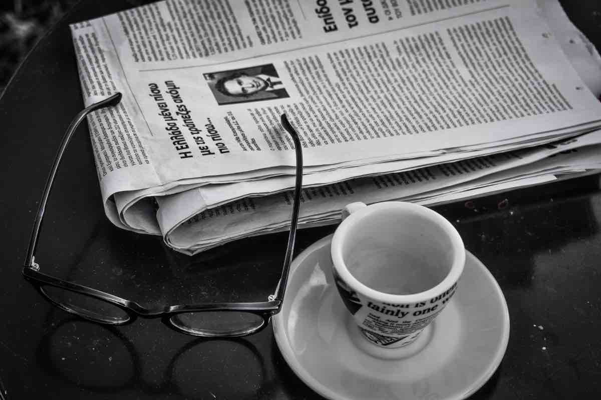 un giornale appoggiato sul tavolo con caffè e occhiali