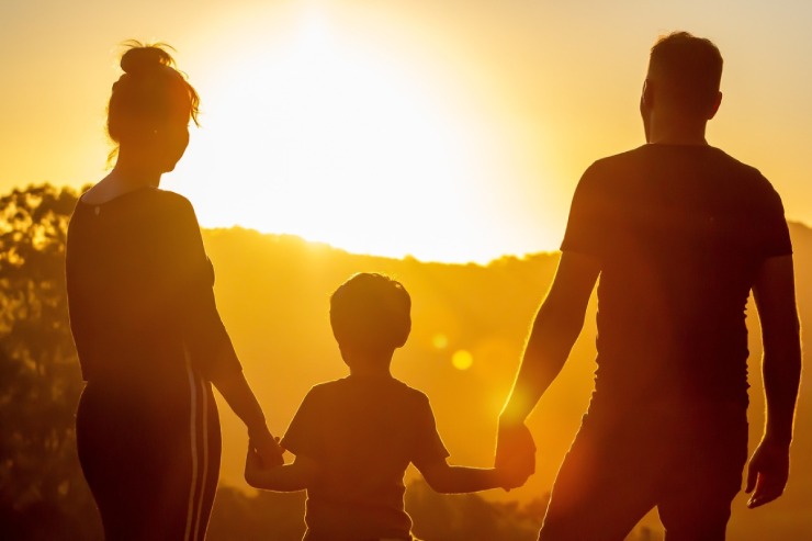 Due genitori e il figlio guardano un tramonto di spalle